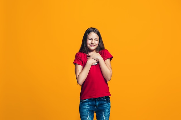 L'adolescente heureuse debout et souriant contre le mur orange