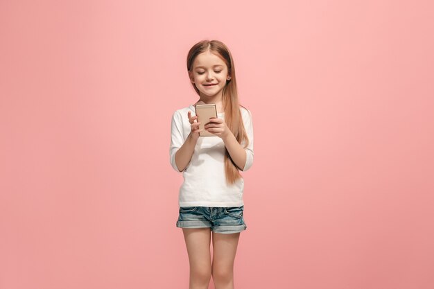 L'adolescente heureuse debout et souriant contre le mur rose