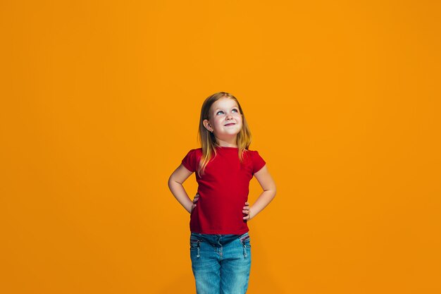 L'adolescente heureuse debout et souriant sur fond orange.