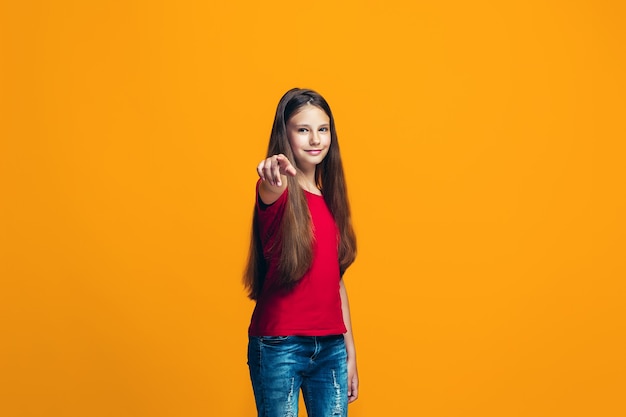 L'adolescente heureuse pointant vers vous, portrait gros plan demi-longueur sur fond orange.