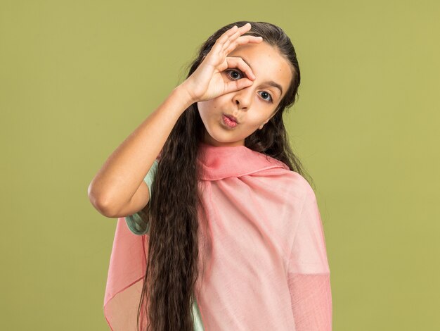 Adolescente impressionnée portant un châle faisant un geste de regard isolé sur un mur vert olive