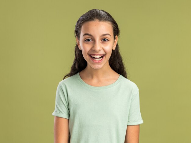 Adolescente joyeuse regardant l'avant en riant isolé sur un mur vert olive