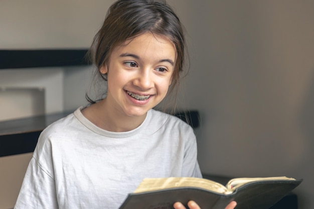 Photo gratuite une adolescente lit un livre et sourit en montrant ses dents avec des appareils dentaires