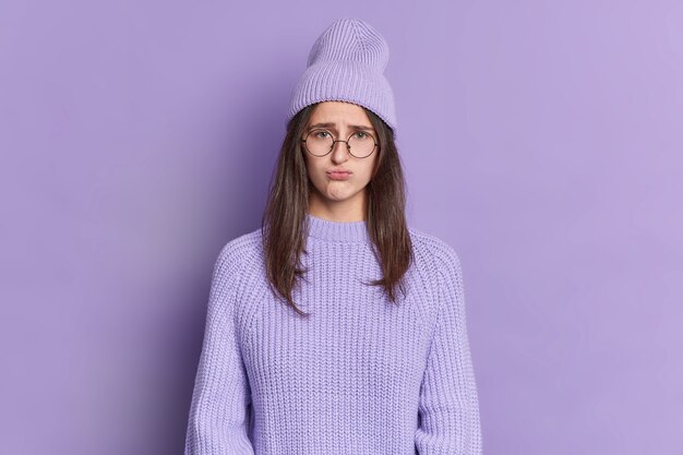 Adolescente mécontente a boudeur expression sombre sacs à main lèvres semble offensé porte de grandes lunettes rondes chapeau et pull.