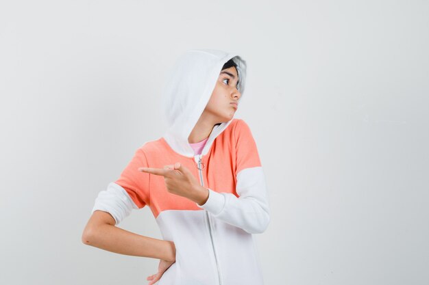 Adolescente pointant vers l'arrière en veste blanche et à la recherche en désaccord.