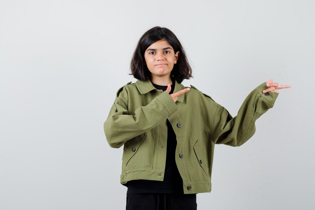 Une adolescente pointant vers la droite dans une veste verte de l'armée et l'air gaie, vue de face.