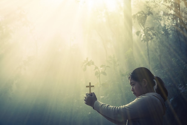 Adolescente priant avec croix dans la nature ensoleillée.