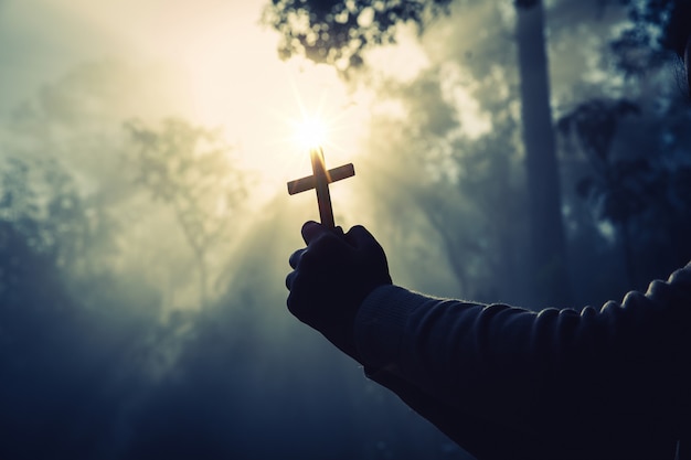 Adolescente priant avec croix dans la nature ensoleillée.