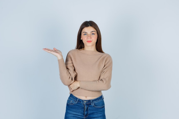 Adolescente en pull, jeans écartant la paume de la main et ayant l'air confiant, vue de face.