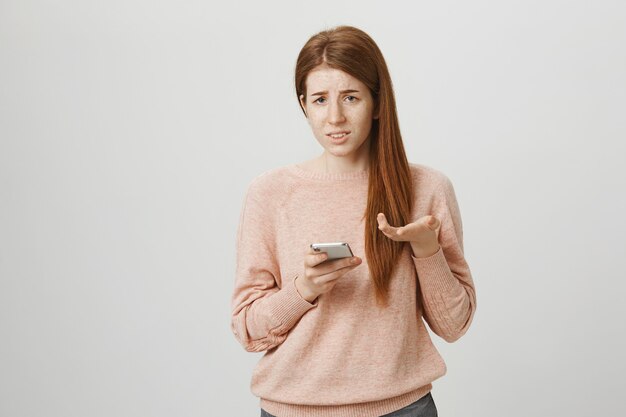 Adolescente rousse confuse haussant les épaules en réaction à un étrange message téléphonique