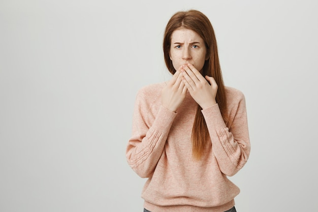 Une adolescente rousse inquiète ferme la bouche et semble inquiète