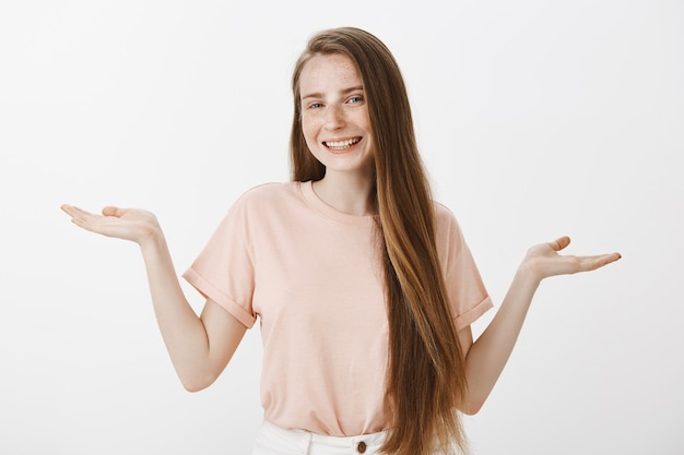 Adolescente souriante désemparée posant contre le mur blanc