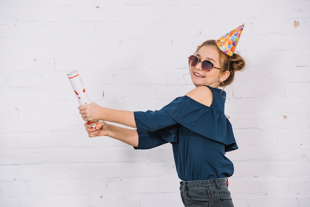 Photo gratuite une adolescente souriante laissant tomber parti popper debout devant le mur blanc