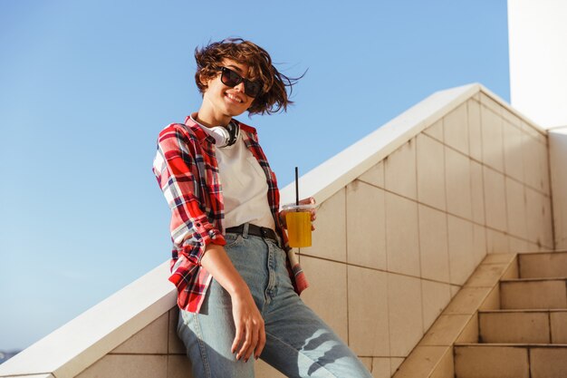 Adolescente souriante à lunettes de soleil boire du jus d'orange