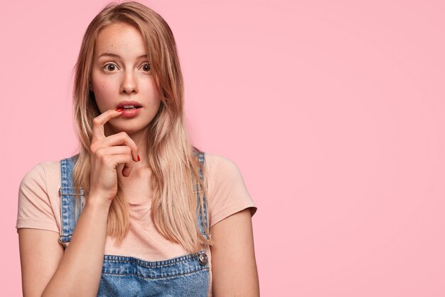 Une adolescente stupéfaite garde l'index près de la bouche, regarde avec une expression étonnée effrayée, entend quelque chose d'étonnant