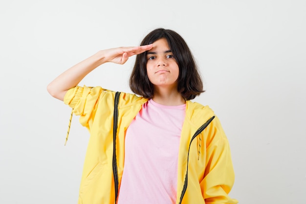 Adolescente en survêtement jaune, t-shirt saluant avec la main sur le front et l'air confiant, vue de face.