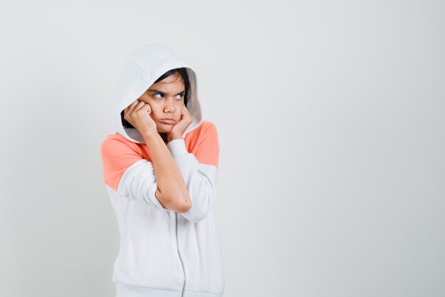 Adolescente en sweat-shirt serrant le visage avec les poings et l'air offensé.