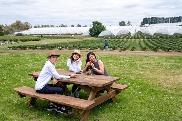 Adolescents branchés et maman se reposent sur un banc en bois à la ferme aux fraises.