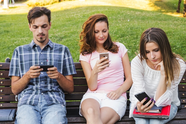 Adolescents avec des smartphoens sur le banc