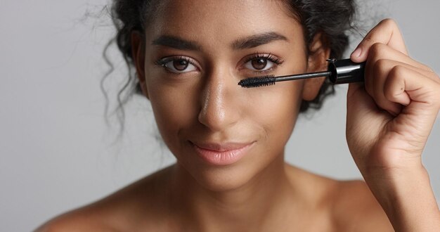 Adorable adolescente du Moyen-Orient avec une belle peau appliquant du mascara sur ses longs cils sur fond blanc