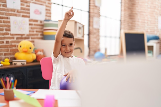 Adorable bambin hispanique assis sur une table ayant une leçon à la maternelle