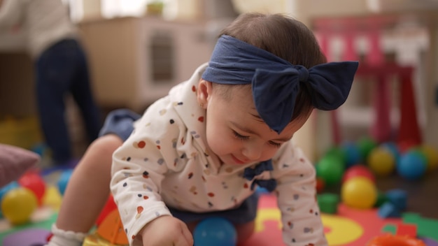 Adorable bambin jouant avec des balles assis sur le sol à la maternelle