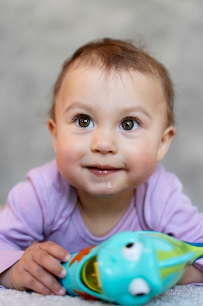 Photo gratuite adorable bébé allongé et jouant sur le sol avec un jouet