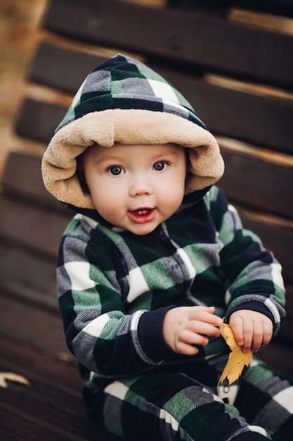 Photo gratuite adorable bébé en salopette chaude avec capuche assis sur feuillage