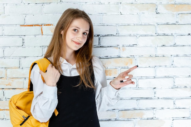 Adorable écolière se dresse sur fond blanc et souriant