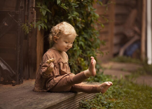 Adorable enfant assis pieds nus sur le porche en mangeant un cookie