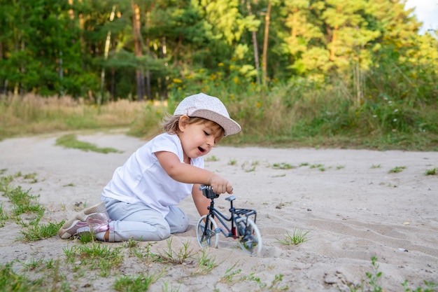 Adorable enfant en bas âge joue avec un vélo jouet dans la nature enfant à quatre pattes dans le sable sur la pelouse