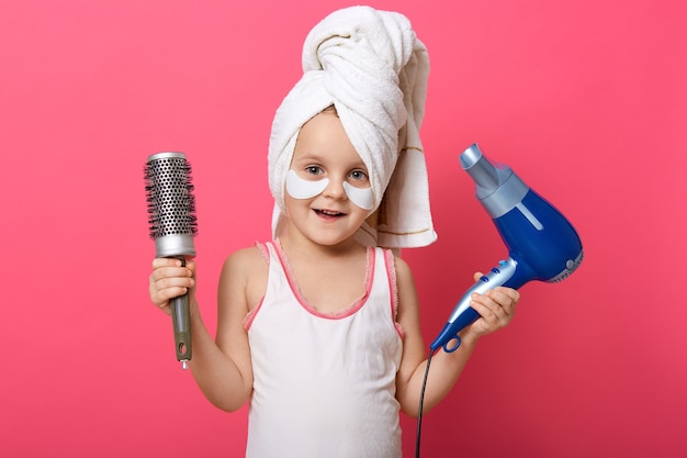 Adorable enfant de sexe féminin tenant un sèche-cheveux et un peigne dans les mains