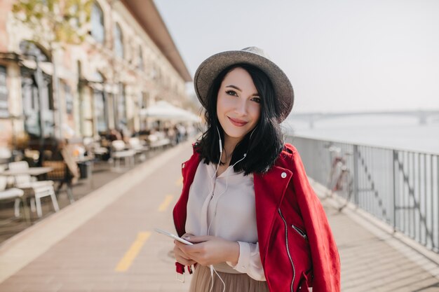 Adorable femme aux cheveux courts tout droit écoutant de la musique au quai en journée ensoleillée