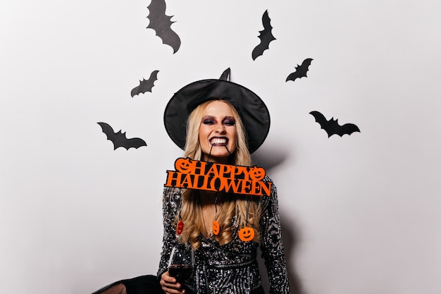 Adorable Femme Aux Cheveux Longs Posant à L'halloween Avec Des Chauves-souris Sur Le Mur. Merveilleuse Fille De Sorcière S'amusant Au Carnaval.