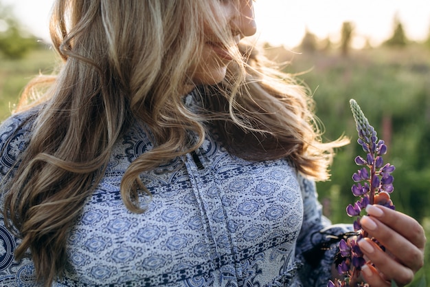 Adorable femme blonde en robe bleue traverse le champ de fleurs de lavande violettes