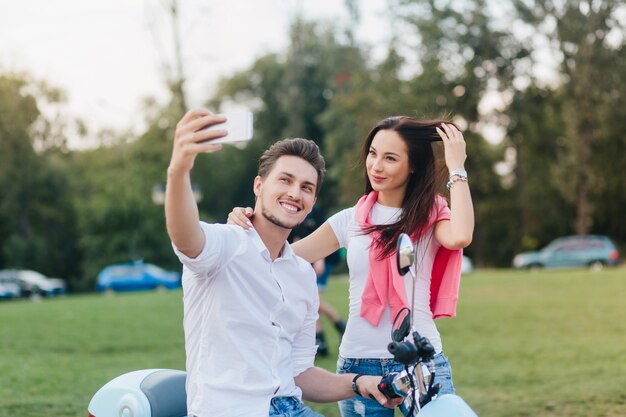 Adorable femme brune joue avec ses longs cheveux pendant que son petit ami la prend en photo