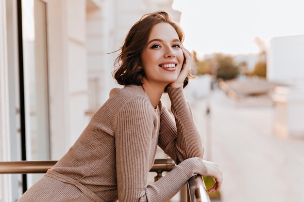 Adorable fille aux yeux noirs riant au balcon. Photo de femme caucasienne joyeuse avec beau sourire.