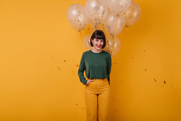 Adorable fille avec des ballons posant avec la main dans la poche. Portrait de la belle femme brune souriant à la fête.