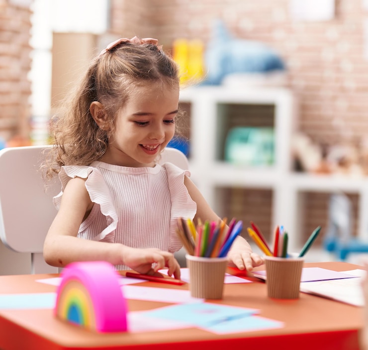 Photo gratuit adorable fille caucasienne assise sur une table dessinant sur papier en classe