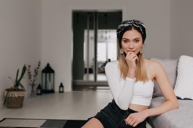 Photo gratuite adorable fille élégante aux cheveux blonds avec accessoire dans la tête portant un haut blanc et un short touche ses lèvres et pose à la caméra tout en se reposant à horm