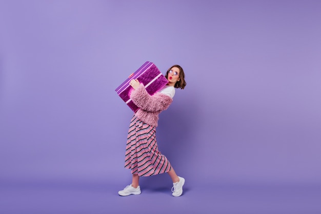 Adorable jeune femme en baskets blanches posant avec boîte cadeau. fille fascinante faisant le visage de baiser exprimant tout en tenant un gros cadeau.