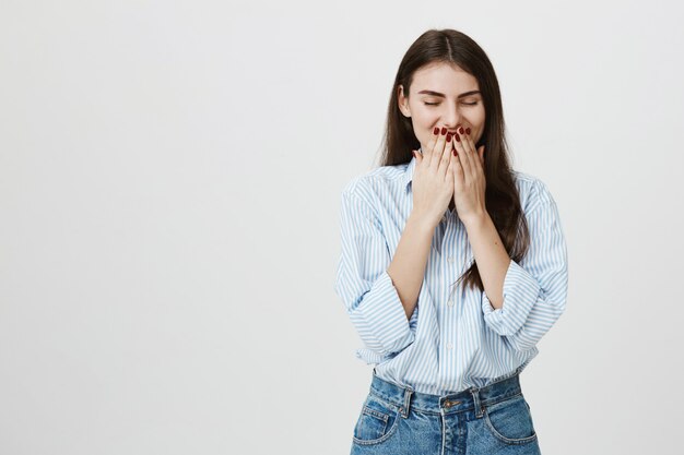 Adorable jeune femme rire, couvrir le sourire avec les mains