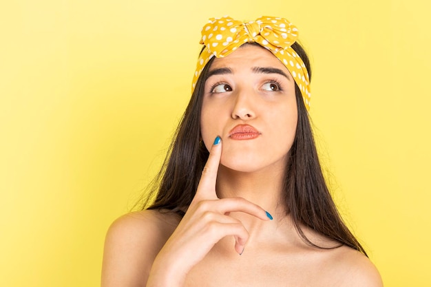 Adorable jeune fille debout sur fond jaune et pensant