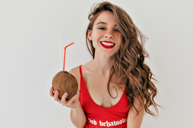 Adorable jolie femme aux longs cheveux brun clair avec du rouge à lèvres rouge porte un maillot de bain rouge avec de la noix de coco