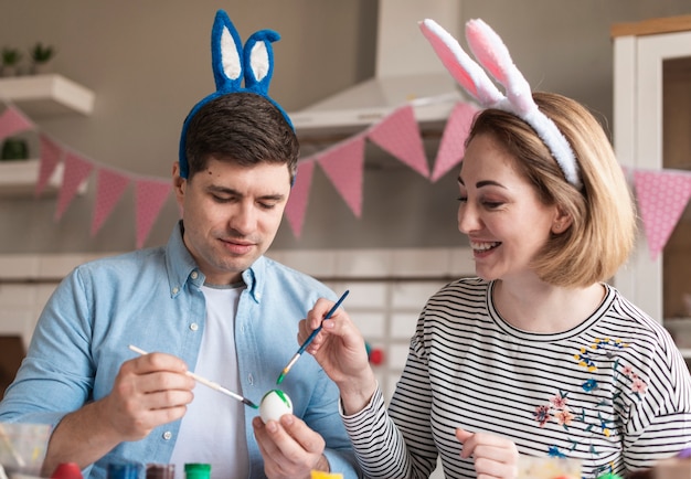 Adorable père et mère peignant des oeufs pour Pâques