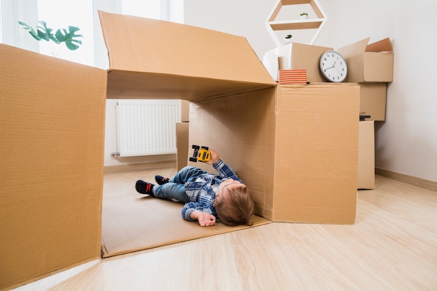 Adorable petit garçon allongé dans la boîte en carton jouant avec une voiture à la maison