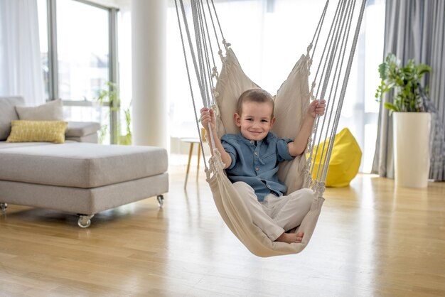 Adorable petit garçon assis sur le hamac dans la maison