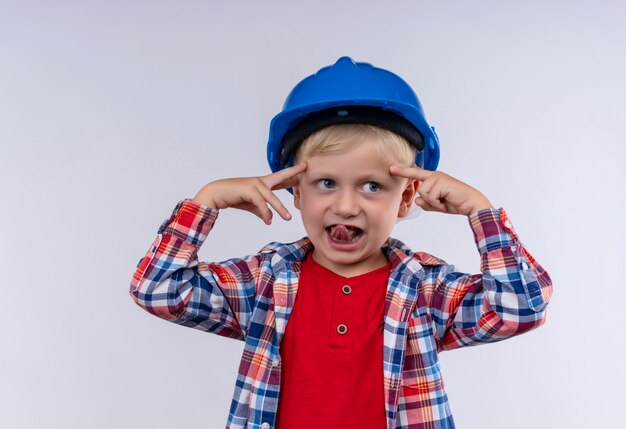 Un adorable petit garçon aux cheveux blonds portant une chemise à carreaux en casque bleu pointant sur sa tête avec l'index