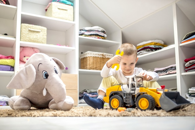 Adorable petit garçon jouant avec des jouets assis par terre dans sa salle de jeux