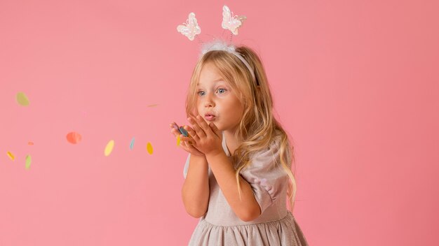 Adorable petite fille en costume soufflant des confettis